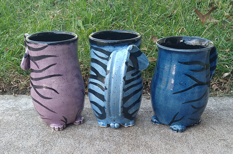 Three cat butt mugs, one purple, one light blue, and one dark blue on a grassy background.