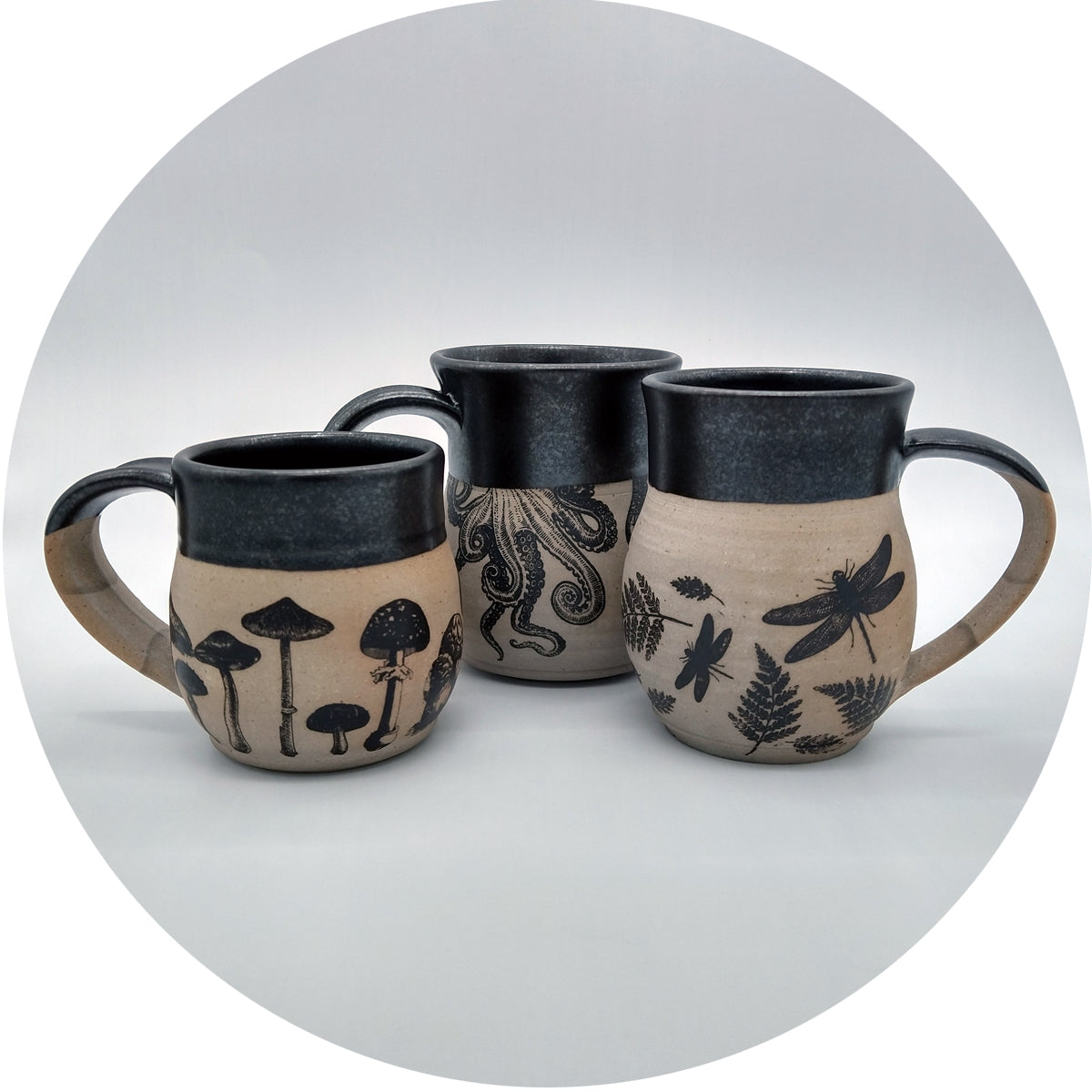 Three mugs made of light clay, decorated with underglaze transfers and glazed on the inside and top with matte black glaze.